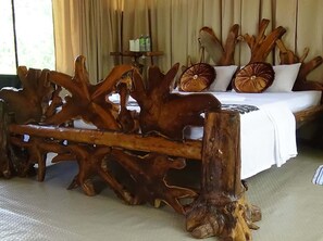 Una cama con una colcha blanca y dos almohadas, rodeada por un cabecero de madera con un diseño natural y original.