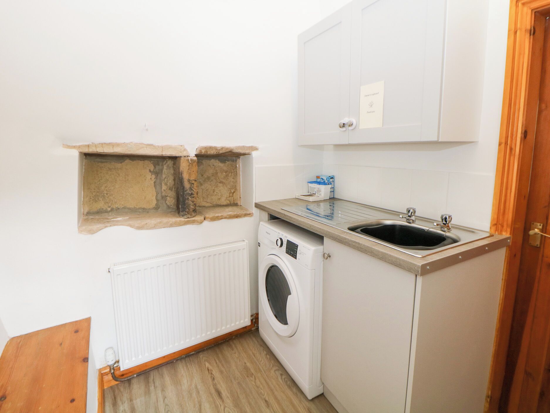 Een kleine keuken met een wasmachine, een spoelbak en een kast.