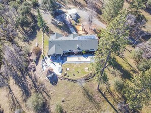 An aerial view of a house with a large deck, solar panels, and a fenced yard.