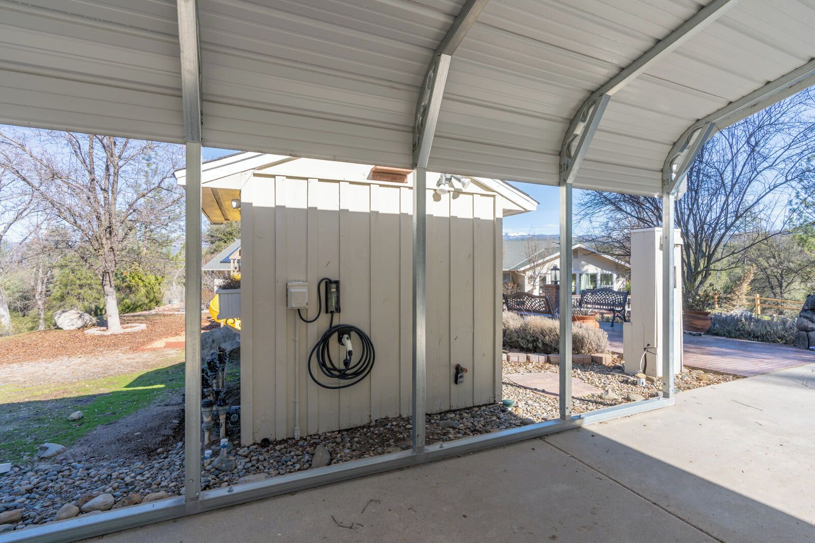A covered outdoor area with a utility box and a coiled cable on a wooden fence.