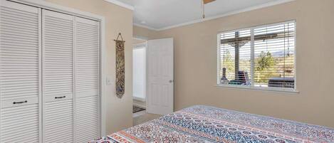 A bedroom with a bed, a ceiling fan, a window with blinds, and a door leading to another room.