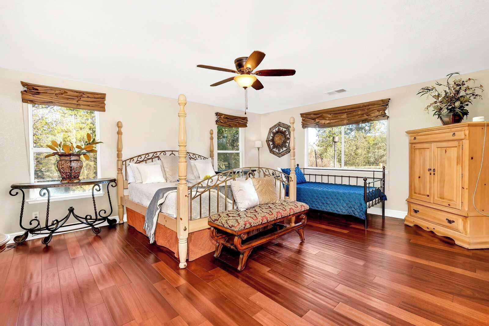 A bedroom with a four-poster bed, a bench, a wooden cabinet, and a ceiling fan.