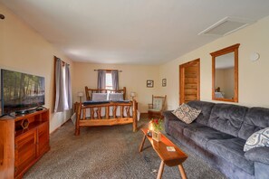 A cozy room with a wooden bed, a sofa, a TV, and a small table with a vase. - Wyandot Woods - Lake House (Laurelville)