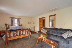 A room with a wooden bed, a dark sofa, a small table with a lamp and flowers, and a mirror on the wall.