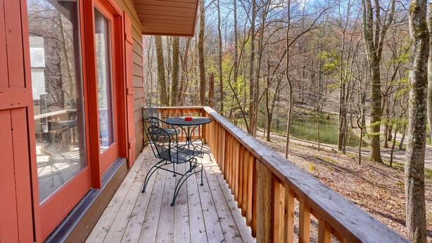 A wooden deck with a table and chairs, overlooking a forested area and a body of water.