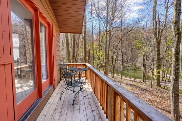 A wooden deck with a table and chairs, overlooking a forested area and a body of water.