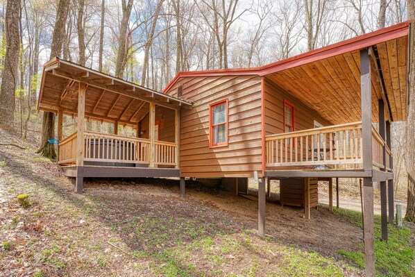 A wooden cabin with a porch and a red roof, surrounded by trees.