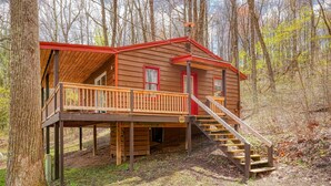 A wooden cabin with a red roof, a wooden deck, and a staircase leading to the entrance.