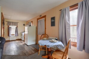 A compact kitchen with a refrigerator, a dining table with chairs, and a window with curtains.