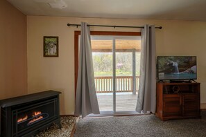A living room with a fireplace, a television on a wooden stand, and a sliding glass door leading to an outdoor deck.