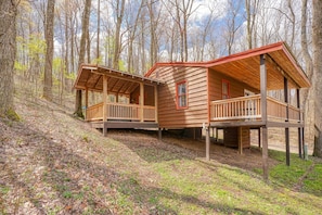 A wooden cabin with a porch and a deck, surrounded by trees.