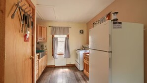 A compact kitchen with wooden cabinets, a white refrigerator, and a window with curtains.