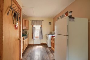A compact kitchen with wooden cabinets, a white refrigerator, and a window with curtains.