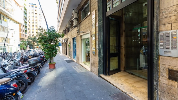Une rue bordée de motos garées, un arbre en pot et un immeuble doté de grandes fenêtres et d’une porte.