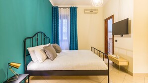 Une chambre à coucher comprenant un lit, une table de chevet, un téléviseur fixé au mur et une fenêtre avec des rideaux.