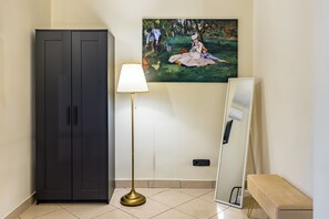 Um quarto com um guarda-roupa escuro, um candeeiro de chão, um quadro, um espelho e um banco.