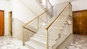 Un escalier avec des rampes en métal et des mains courantes en bois, menant à un sol carrelé orné d’un motif en mosaïque.