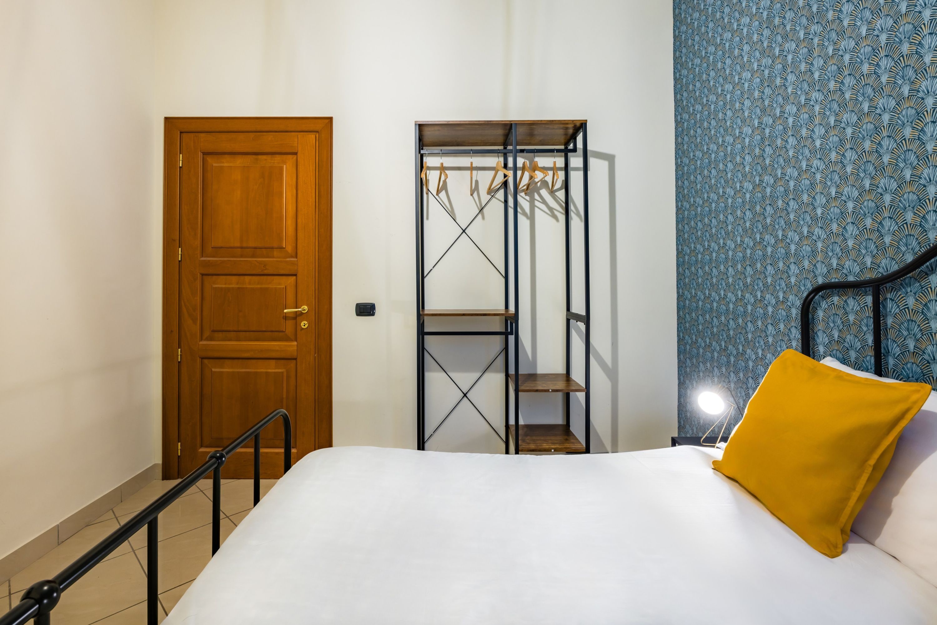 Un dormitorio con cama, puerta de madera, armario metálico y pared con diseño.
