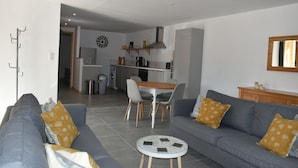 Een moderne woonkamer met een grijze bank, een klein rond salontafeltje en een eethoek met een tafel en stoelen.