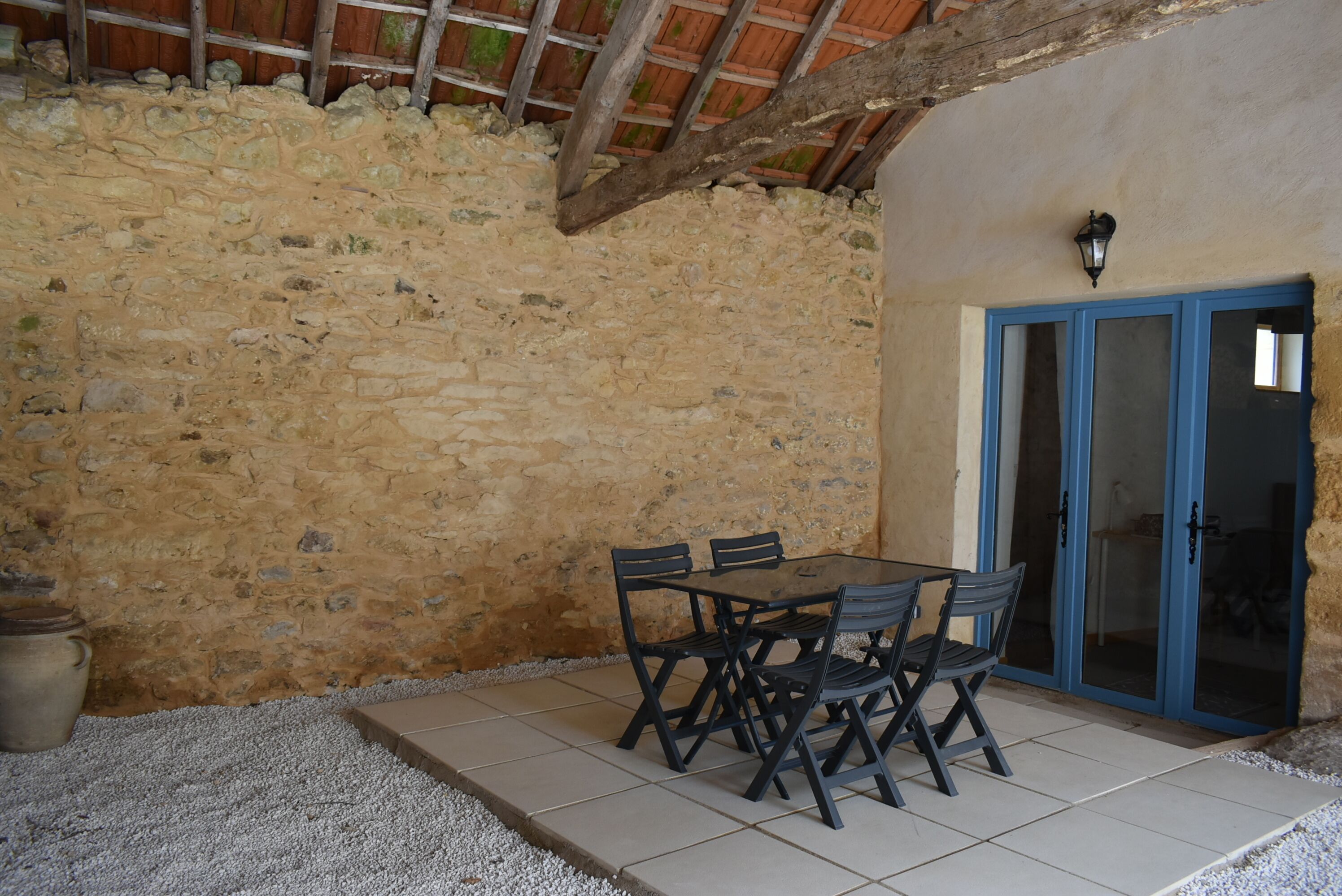 A stone-walled patio with a table and chairs, a blue door, and a tiled floor.