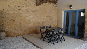 Een terras met stenen muren, een tafel, stoelen, een blauwe deur en een betegelde vloer.