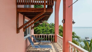 A balcony with stone flooring, two lounge chairs, a small table, and a view of the sea. - Kayak, Snorkel, Dive Waterfront 2BR 2BA  A/C
Beautiful Quiet Caribe bight w/pool (Jonesville Point)