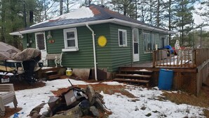 A green cabin with a deck, surrounded by trees and snow. - Quaint Cottage on a Popular Lakefront, Dock, Fire pit. (Kinmount)