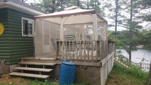 A cabin with a covered deck and a blue barrel. - Quaint Cottage on a Popular Lakefront, Dock, Fire pit. (Kinmount)