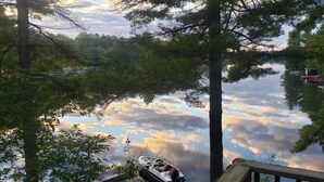 A tranquil lake with boats docked, surrounded by dense trees and a clear sky. - Quaint Cottage on a Popular Lakefront, Dock, Fire pit. (Kinmount)