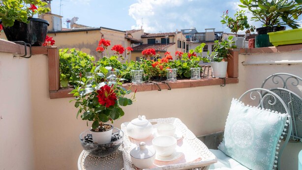 Eine Dachterrasse mit Blumentöpfen, einem Tisch mit Teekannen und Tassen sowie einem Stuhl.