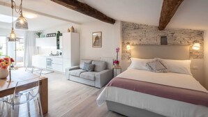 Ein modernes Schlafzimmer mit einem großen Bett, einem Holzbalken an der Decke, einer Steinwand und einer kleinen Küchenzeile im Hintergrund.