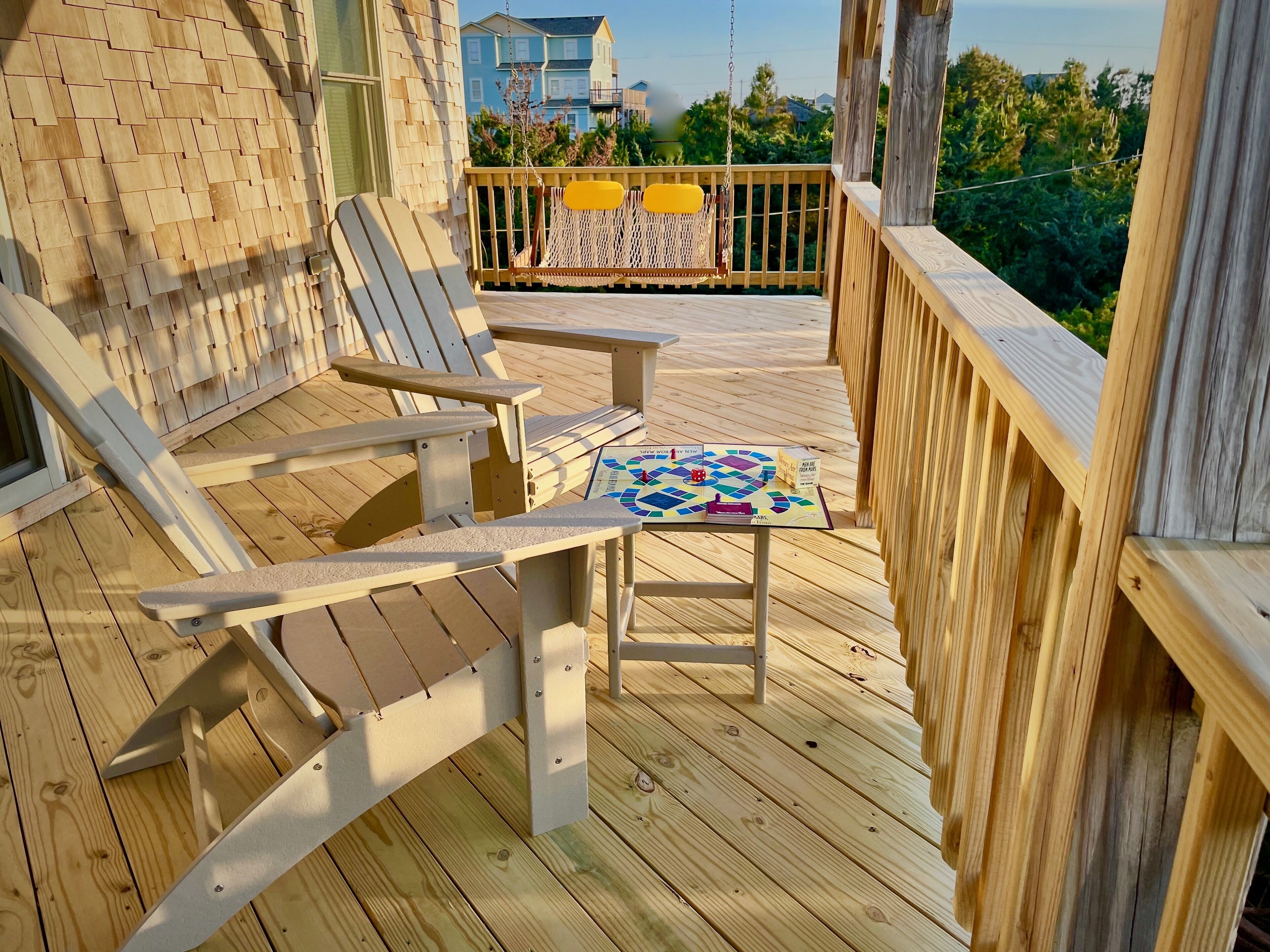 A wooden deck with Adirondack chairs and a table with a board game.