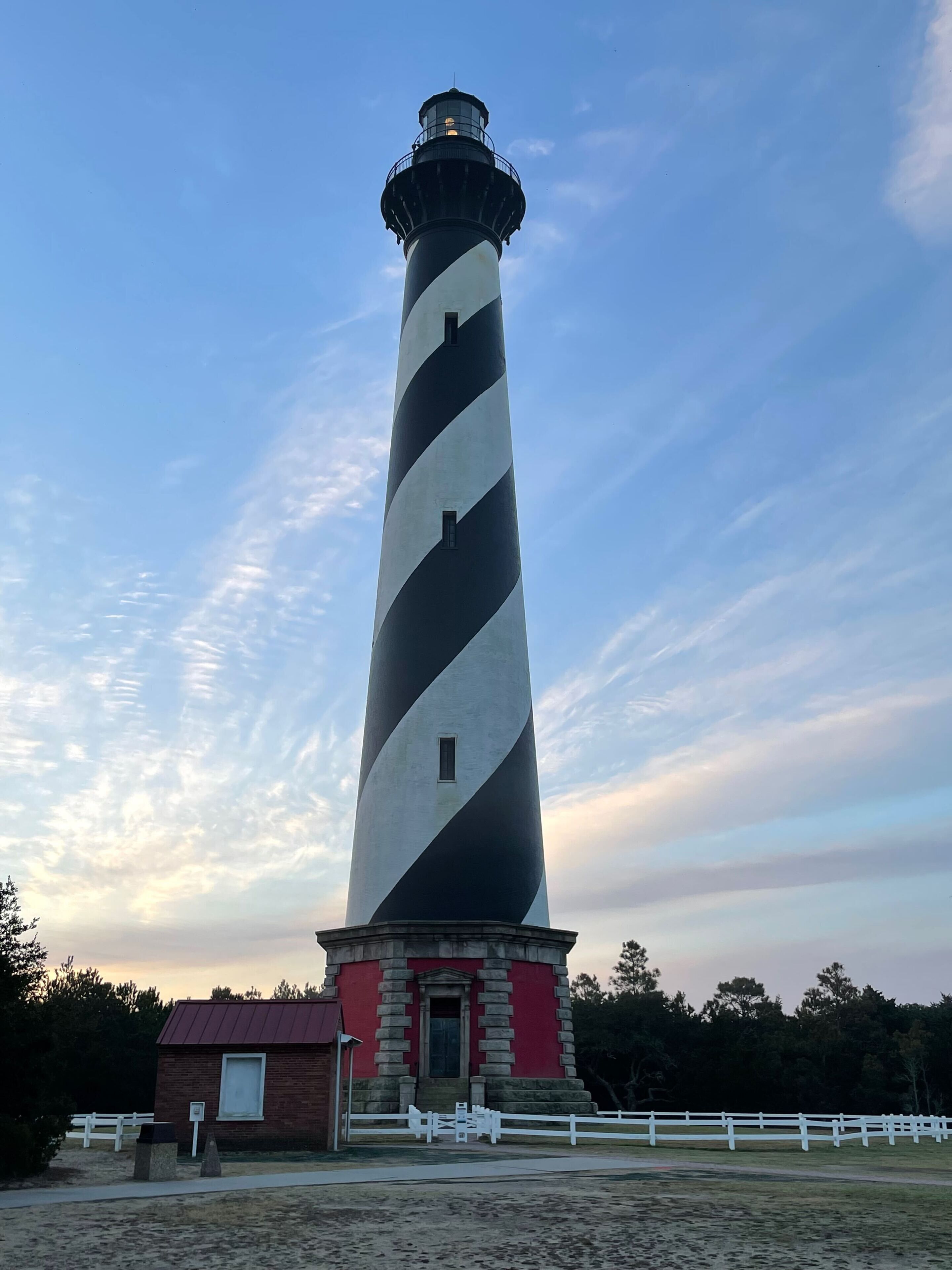 A tall lighthouse with a black and white striped pattern, a brick base, and a red roof.