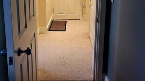 A hallway with a carpeted floor leading to a white door with a doorknob and a small rug at the entrance. - Captivating 2-bed Apartment in Winchester (Winchester)
