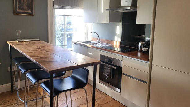 A modern kitchen with a wooden table, black bar stools, and stainless steel appliances. - Captivating 2-bed Apartment in Winchester (Winchester)