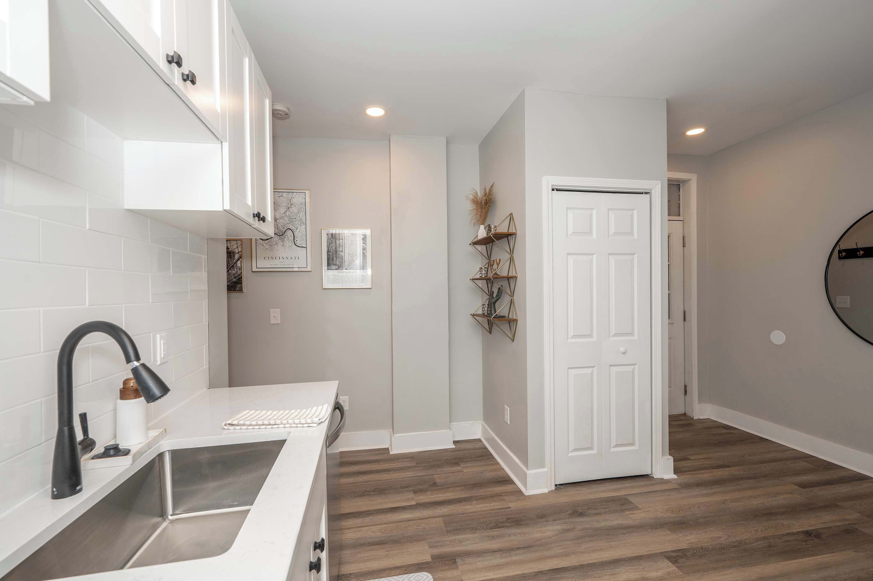 A modern kitchen with white cabinets, a stainless steel sink, and a wooden floor.