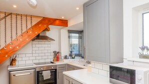 Une cuisine moderne avec un escalier en bois, des appareils électroménagers en acier inoxydable et une grande fenêtre équipée de stores.
