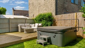 Un jardin avec un jacuzzi, des meubles en osier et une terrasse en bois.