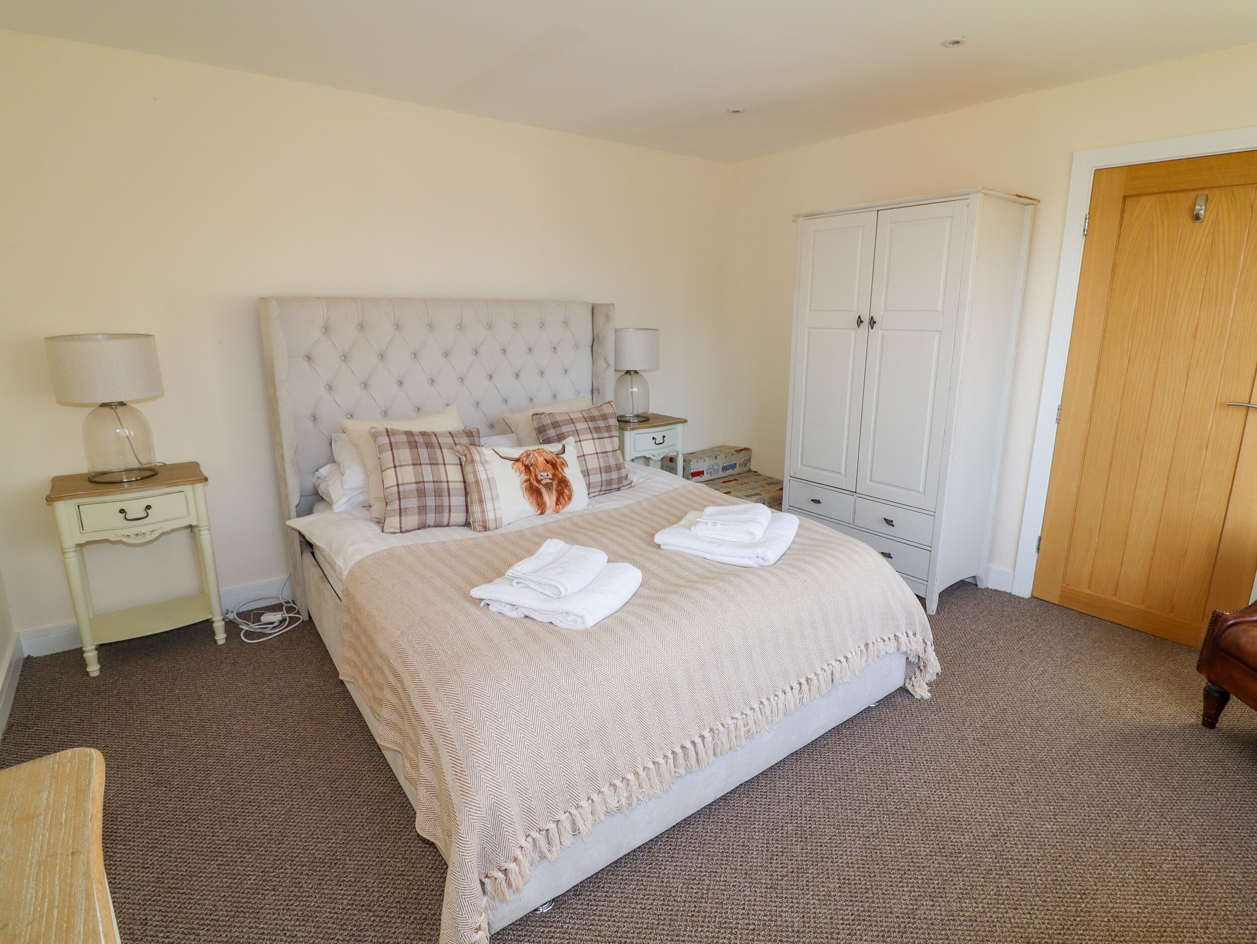 A neatly arranged bedroom with a large bed, a wardrobe, and a bedside table with a lamp.