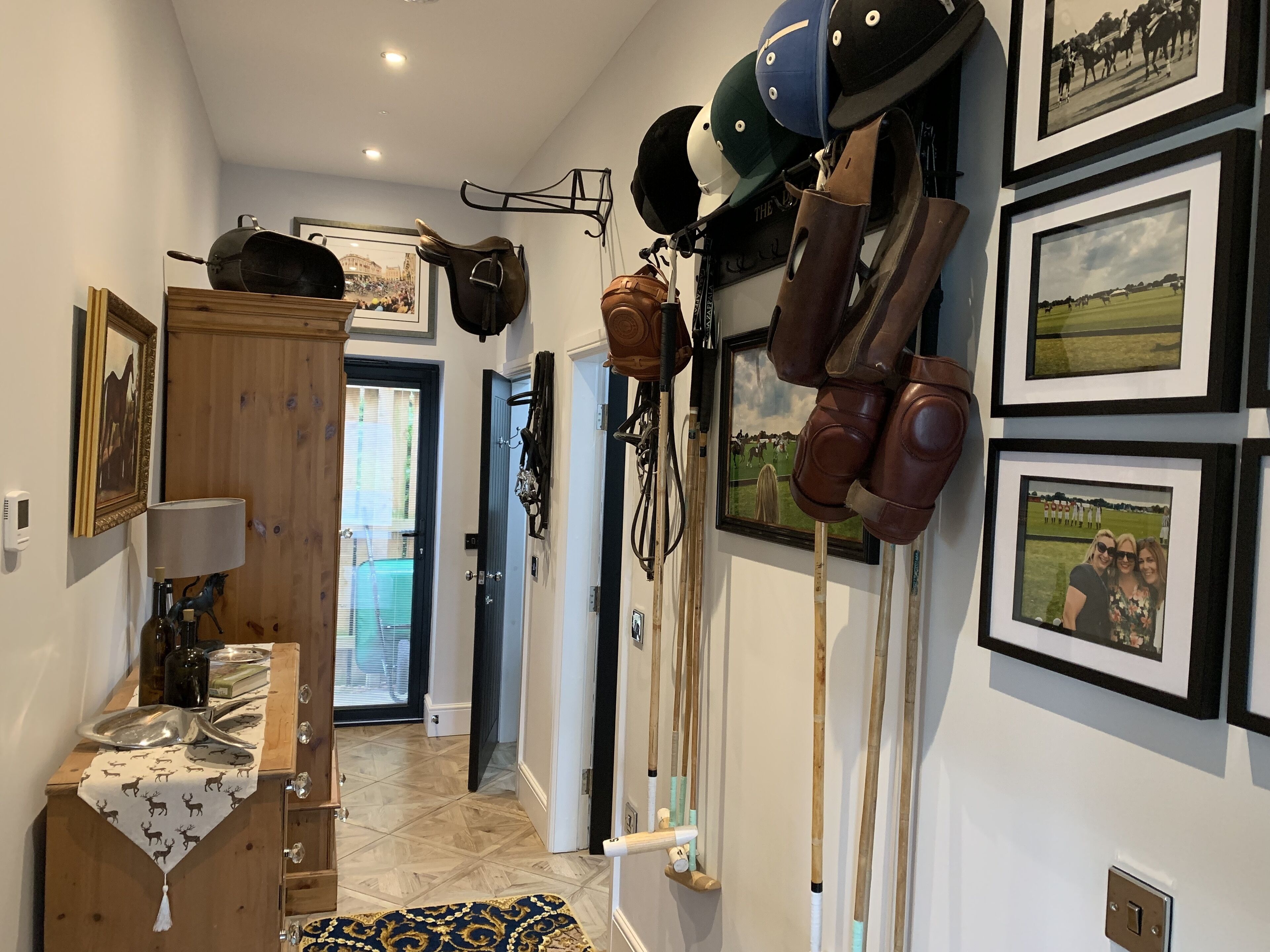 A hallway with horse riding equipment, framed photos, and a wooden cabinet.