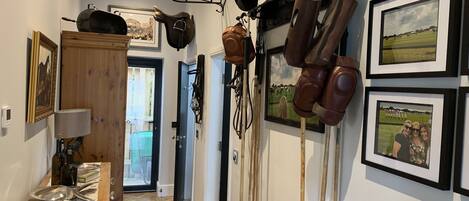 A hallway with horse riding equipment, framed photos, and a wooden cabinet.