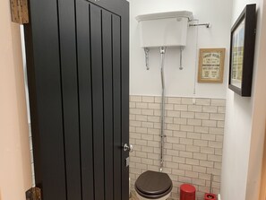 Un baño pequeño con inodoro, tanque blanco y cesto de basura rojo.