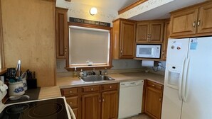 A compact kitchen with wooden cabinets, a microwave, a refrigerator, and a stove. - Loon Lodge Limit 8 3 Bedroom Home by RedAwning (Standish)