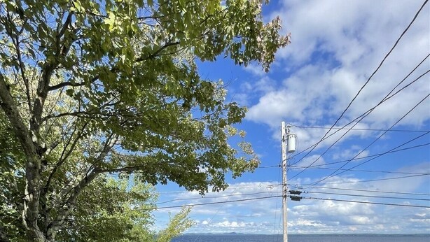 A wooden deck with a glass table and two chairs, overlooking a body of water with boats and a dock. - Loon Lodge Limit 8 3 Bedroom Home by RedAwning (Standish)