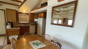 A dining area with a wooden table and chairs, a kitchen in the background, and a large mirror on the wall. - Loon Lodge Limit 8 3 Bedroom Home by RedAwning (Standish)