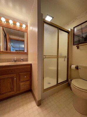 A bathroom with a wooden vanity, a glass shower enclosure, and a toilet. - Loon Lodge Limit 8 3 Bedroom Home by RedAwning (Standish)