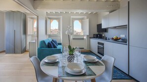 Une cuisine moderne avec des meubles blancs, un coin repas doté d’une table ronde pour quatre personnes, et un canapé bleu en arrière-plan.