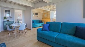 Un salon moderne avec un canapé de couleur turquoise, une table à manger avec des chaises et un coin cuisine visible à travers une porte ouverte.