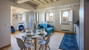 Un salon moderne avec un canapé bleu, un coin repas doté d’une table ronde et de chaises, et un espace cuisine.