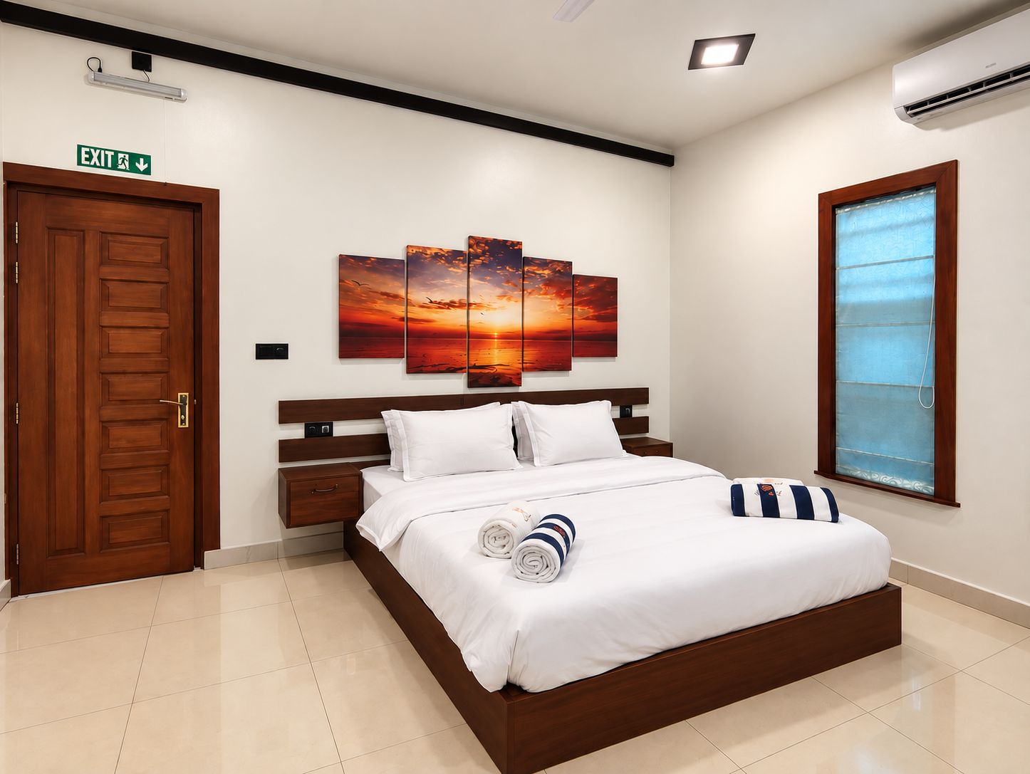 Habitación de hotel con cama, mesita de noche, una obra de arte colgada en la pared, señal de salida y ventana con persianas.